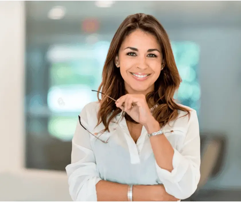 Confident professional woman smiling and holding eyeglasses in a bright, modern office setting