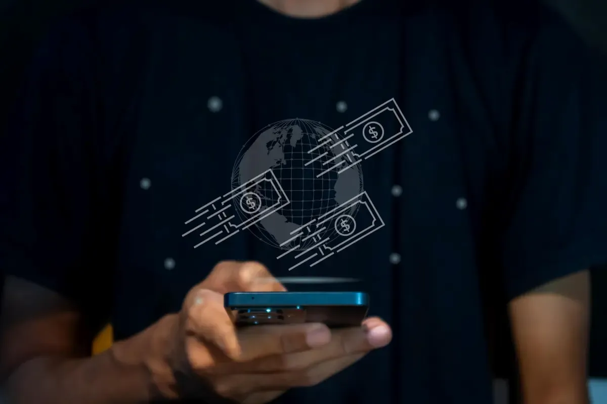Person holding a smartphone with digital illustration of global money transfers, showing currency notes moving around a globe to represent international payments.