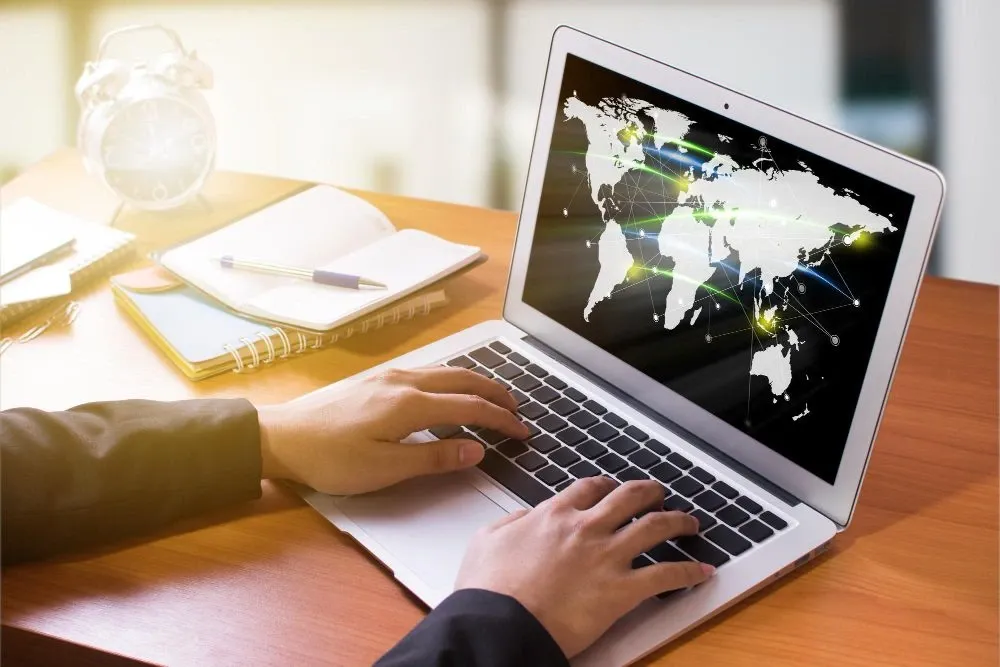Person typing on a laptop displaying a world map with glowing connection points, symbolizing global communication, data flow, or international money transfers.
