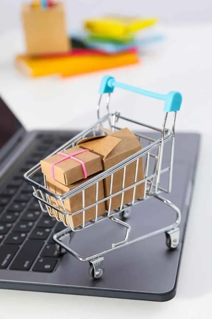Mini shopping cart filled with packages placed on a laptop keyboard, representing online retail and ecommerce.