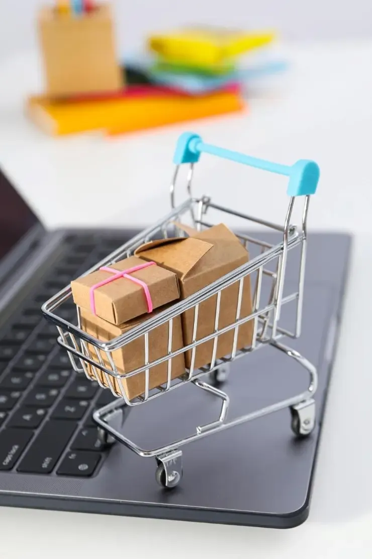 Mini shopping cart filled with packages placed on a laptop keyboard, representing online retail and ecommerce.