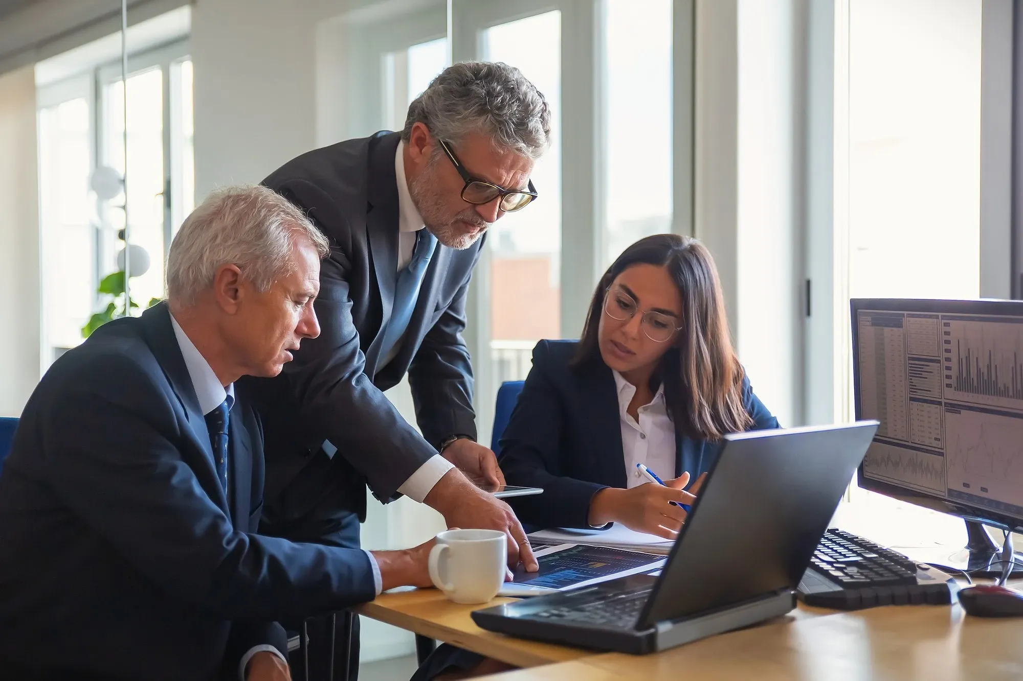 Business professionals reviewing financial data and charts together at a desk, discussing international payment and FX strategy in a modern office setting.