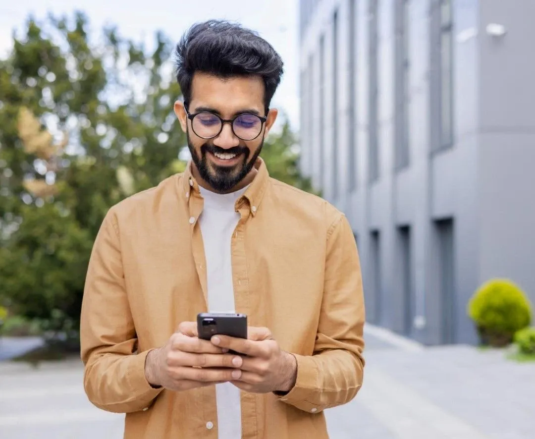 Smiling man standing outside a modern building while using a smartphone, symbolizing convenient and secure mobile money transfer services.