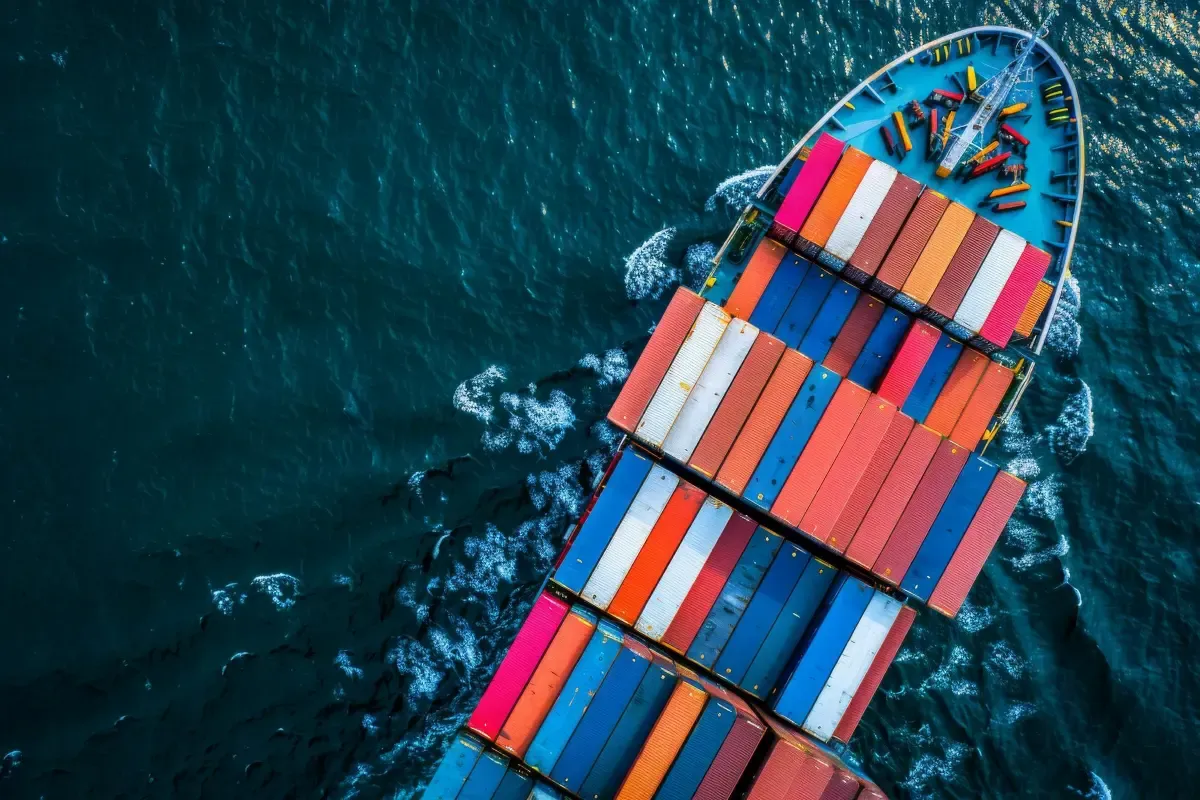 Aerial view of a cargo ship carrying colourful containers across open ocean, representing global trade and international shipping