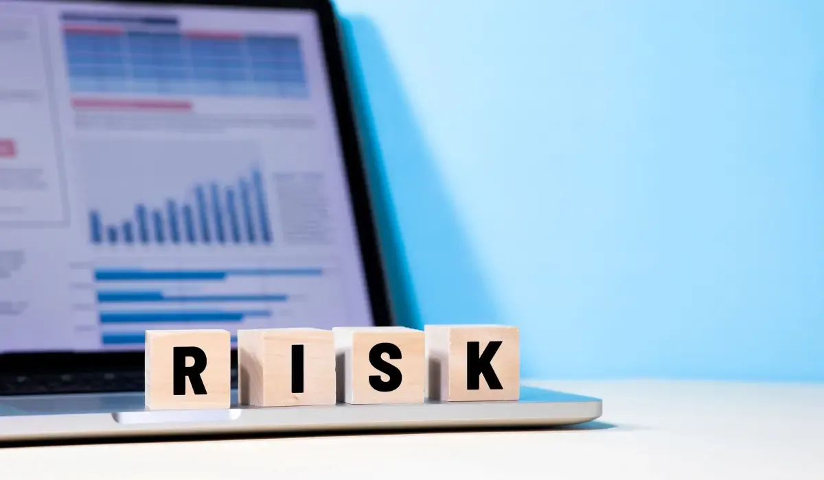 Wooden blocks spelling “RISK” placed in front of a laptop displaying financial charts and data, representing financial and foreign exchange risk management.