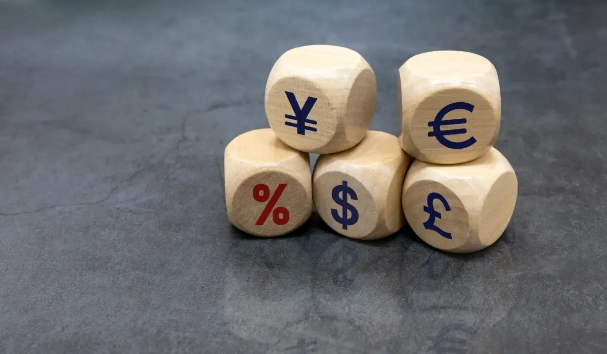Wooden blocks with global currency symbols including dollar, euro, yen, pound, and percentage sign representing exchange rates and international money transfer costs