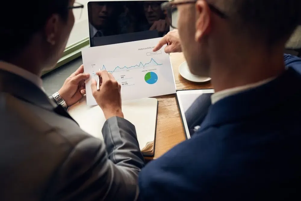 Two professionals analyzing a printed line graph with pie chart.