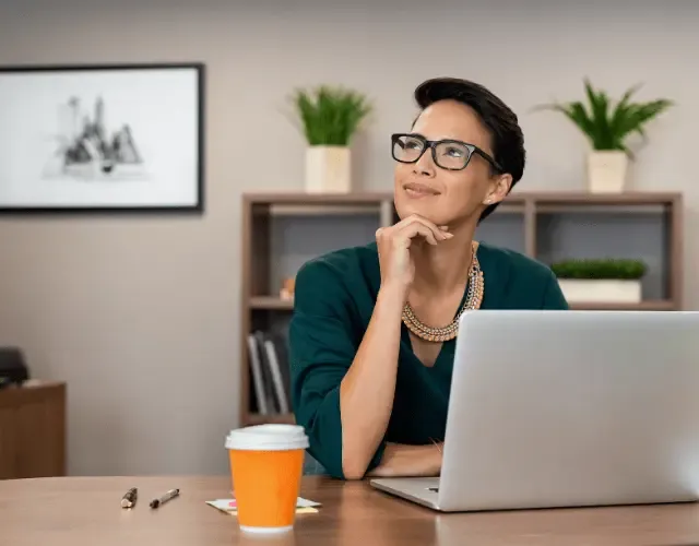 Businesswoman thinking while working at a desk with a laptop and coffee cup