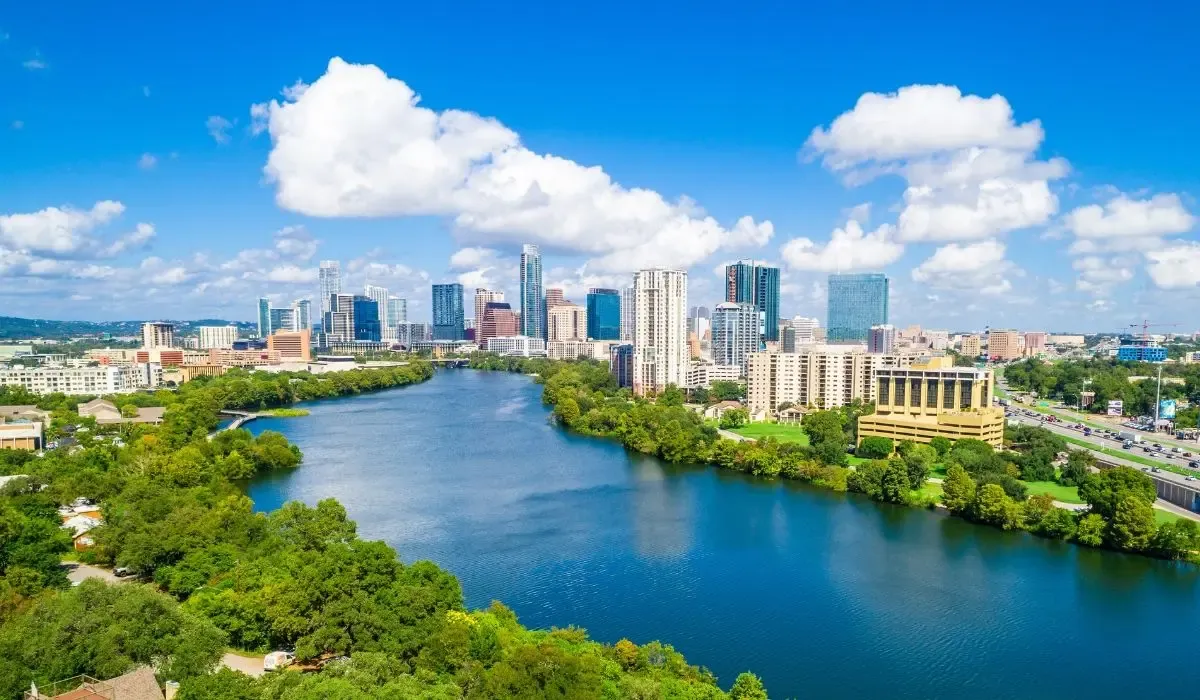 A panoramic view of downtown Austin, Texas, showcasing the skyline with modern high-rise buildings and the Colorado River in the foreground.