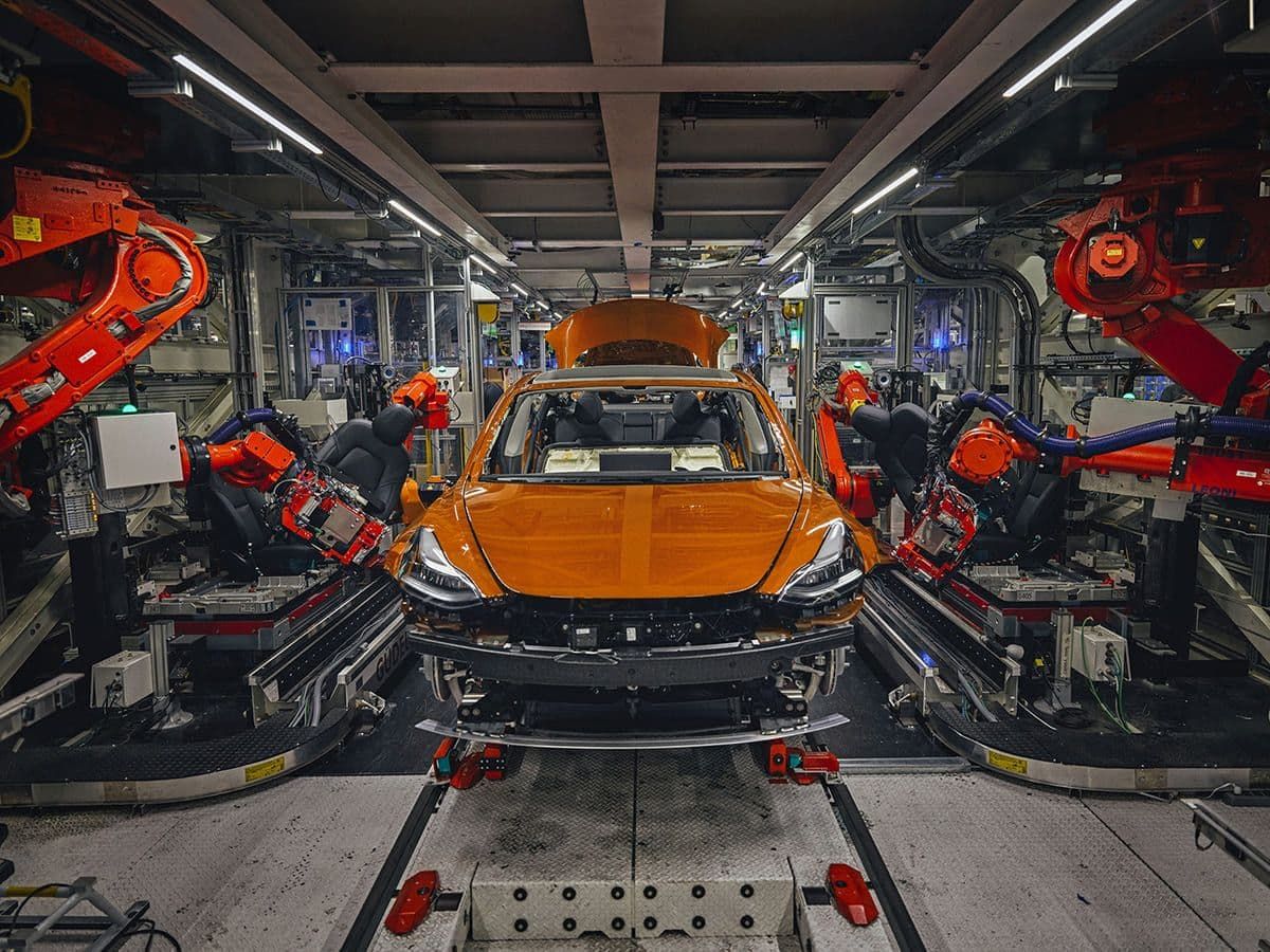 Automated car manufacturing assembly line with robotic arms working on an orange vehicle inside a modern factory.