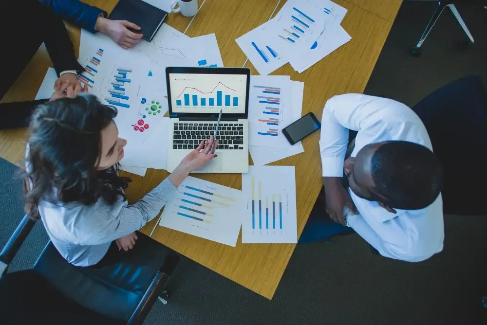 Top-down view of a team meeting with financial documents and a laptop displaying a bar chart during a meeting session.