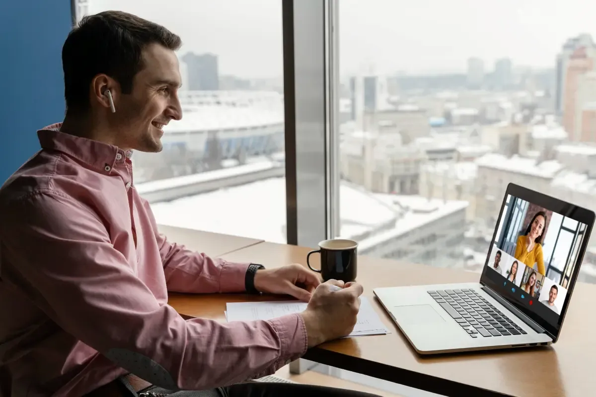 Man attending a virtual business meeting on a laptop while working remotely with city skyline view.