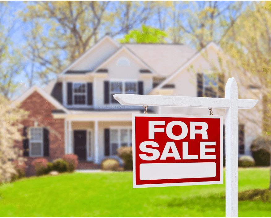 Red and white 'For Sale' sign in front of a suburban two-story house with green lawn and spring trees