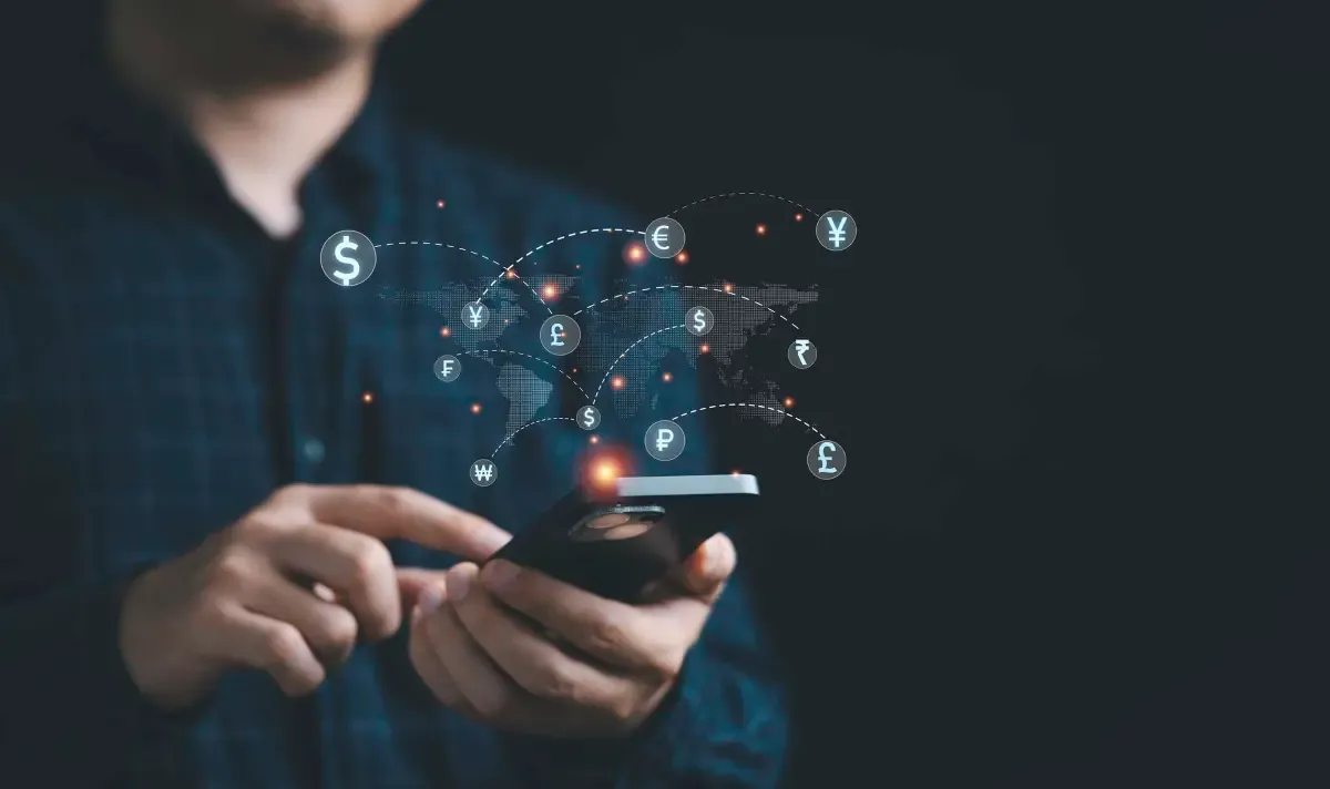 Business professional using a smartphone with a digital world map and floating currency symbols, representing global payments, foreign exchange, and international money transfers.