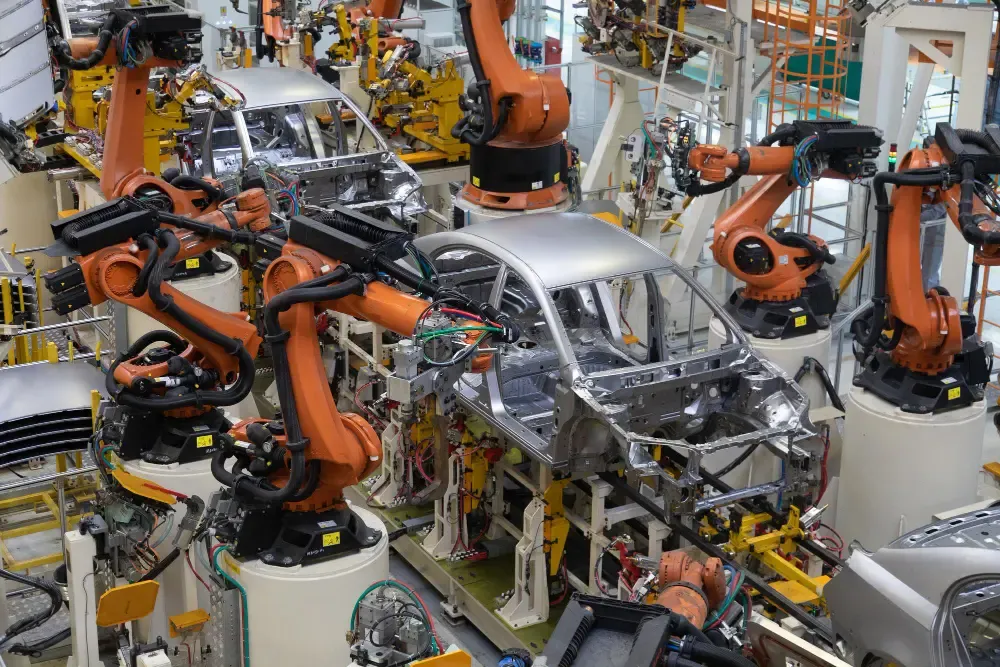 Automated car manufacturing line with robotic arms assembling a silver vehicle body inside a modern automotive factory.