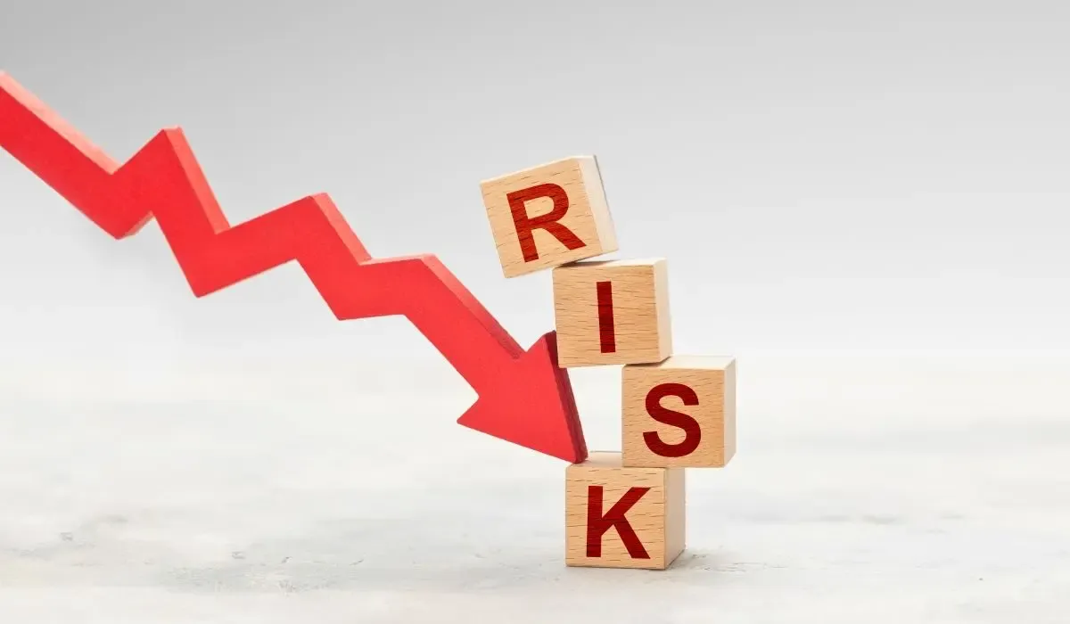 An image of a downward red arrow representing financial or currency risk, knocking over wooden blocks that spell the word 'RISK.