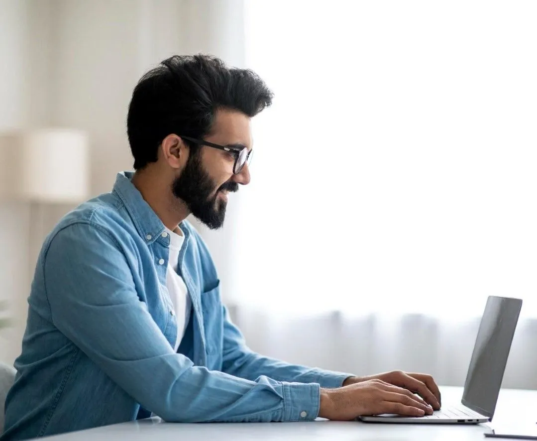 Man sitting at a desk using a laptop, smiling and focused, representing secure and easy online money transfers from home