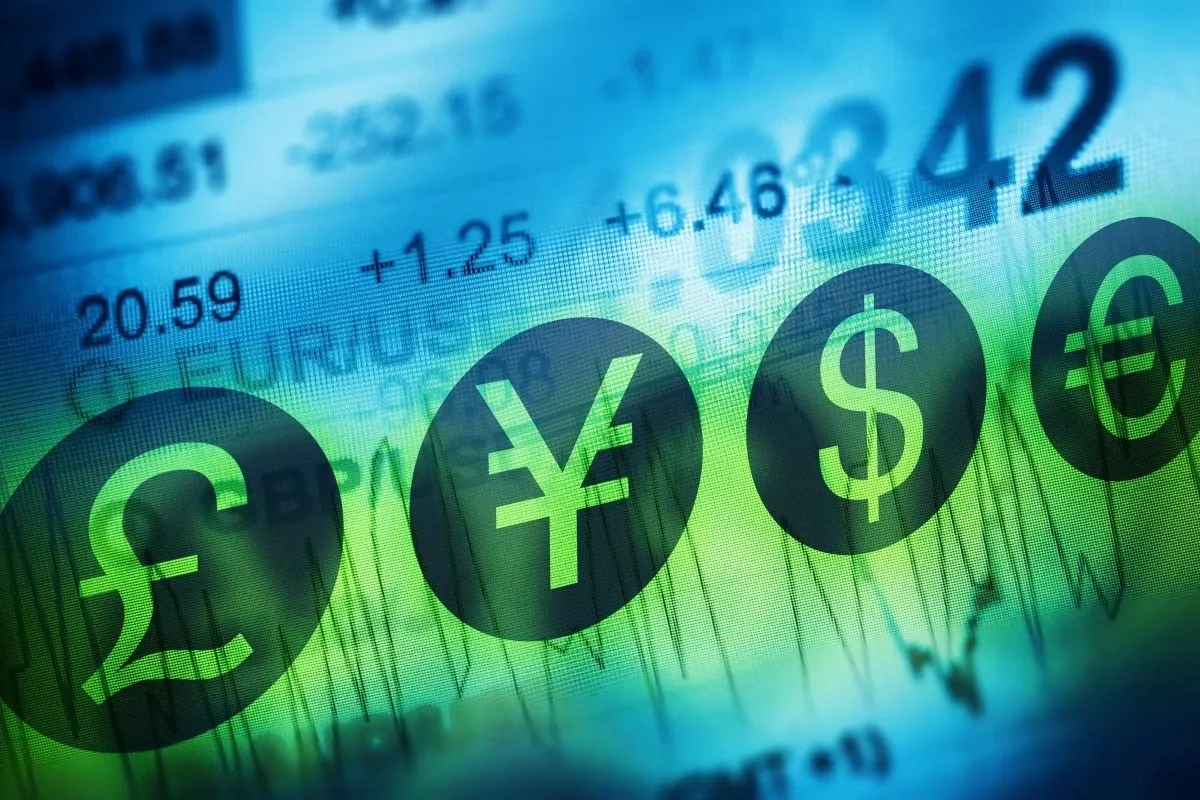 Close-up of global currency symbols displayed over a digital financial chart with fluctuating market data in the background.