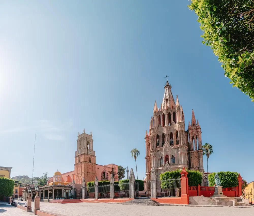 The iconic pink spires of the Parroquia de San Miguel Arcángel overlooking a sun-drenched historic plaza.