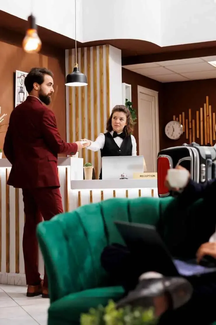 Hotel receptionist greeting a guest at the front desk, showcasing the hospitality industry.