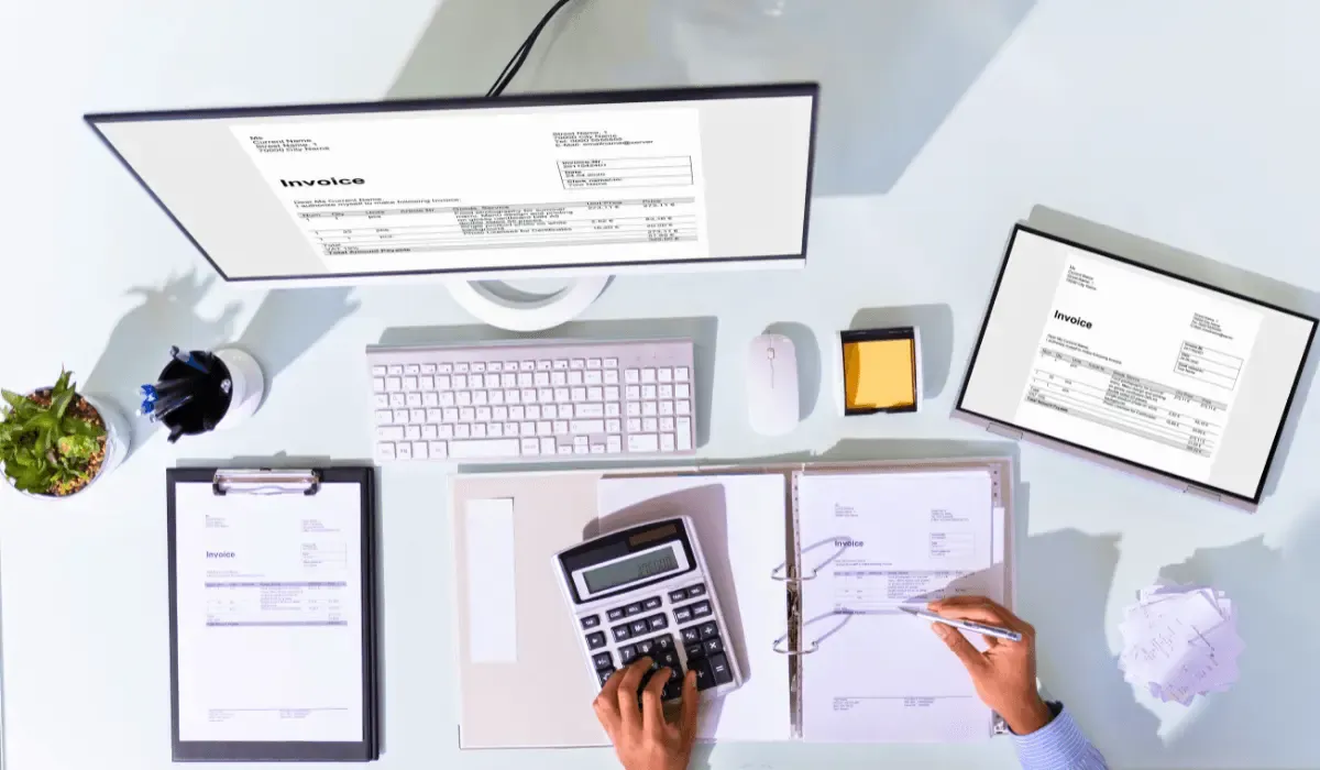 A top-down view of a workspace with invoices, a calculator, a computer, and office supplies.