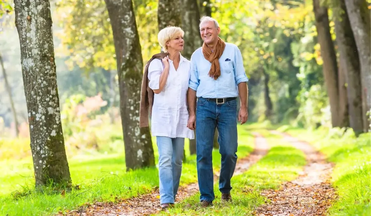 An image of a happy retired couple walking along a scenic, tree-lined path on a sunny day.