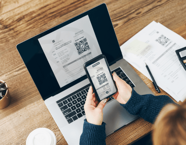 Person scanning a QR code from an invoice using a smartphone in front of a laptop