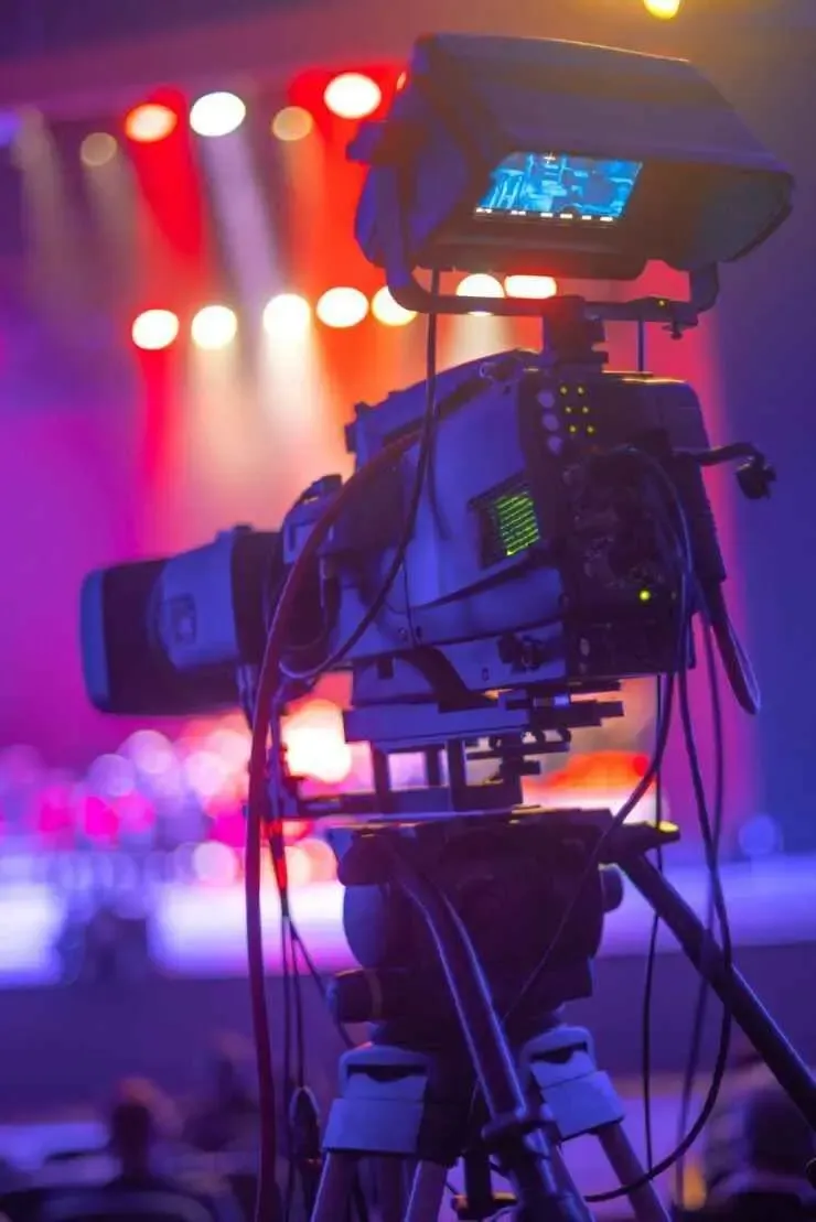 Professional video camera set up at a stage production with lights and background blur, representing media and entertainment industry.