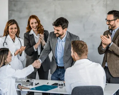 Team of professionals clapping as two colleagues shake hands during a business meeting
