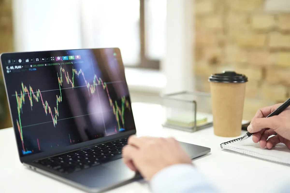 Person reviewing currency charts on a laptop while taking notes