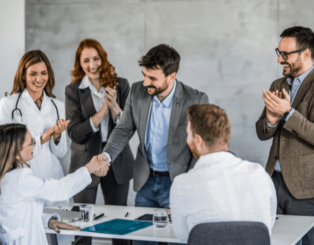 Team of professionals clapping as two colleagues shake hands during a business meeting