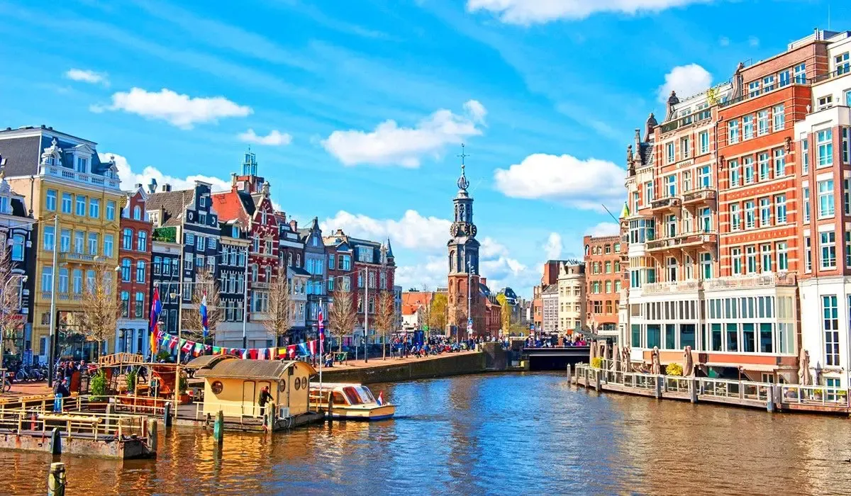 Scenic canal view in Amsterdam, featuring vibrant historic buildings, canal boats, and the famous Munttoren tower under a clear sky.