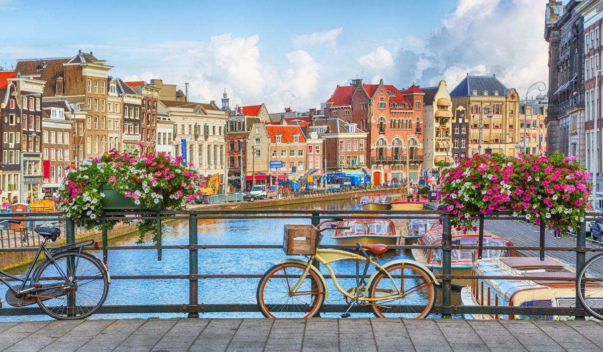 Picturesque bridge in Amsterdam, adorned with colorful flower baskets and parked bicycles, overlooking boats on a lively canal.