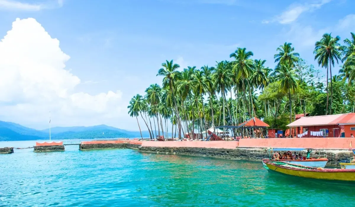 Scenic view of the Andaman Islands in India, featuring turquoise waters, palm trees, colorful buildings, and a small docked boat near the shore.