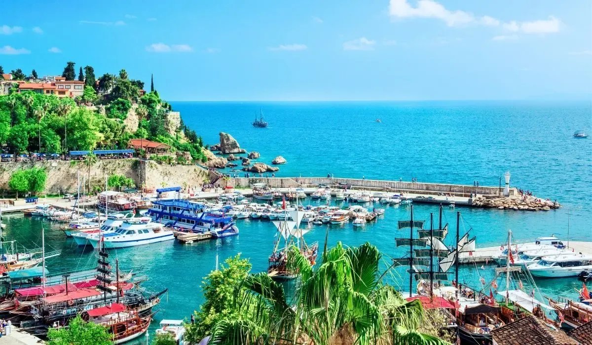 Vibrant harbor scene in Antalya, Turkey with colorful yachts and traditional boats docked along azure waters beside historic cliffs. Canadians exploring property investments in Turkey can access excellent CAD to TRY exchange rates and low-fee payments via MTFX.