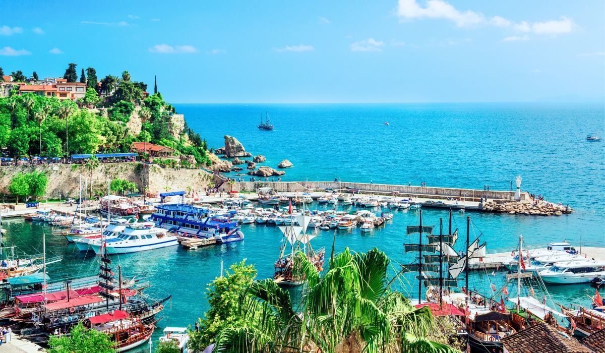 Colorful marina in Antalya, Turkey, filled with boats and surrounded by lush cliffs and historic buildings.