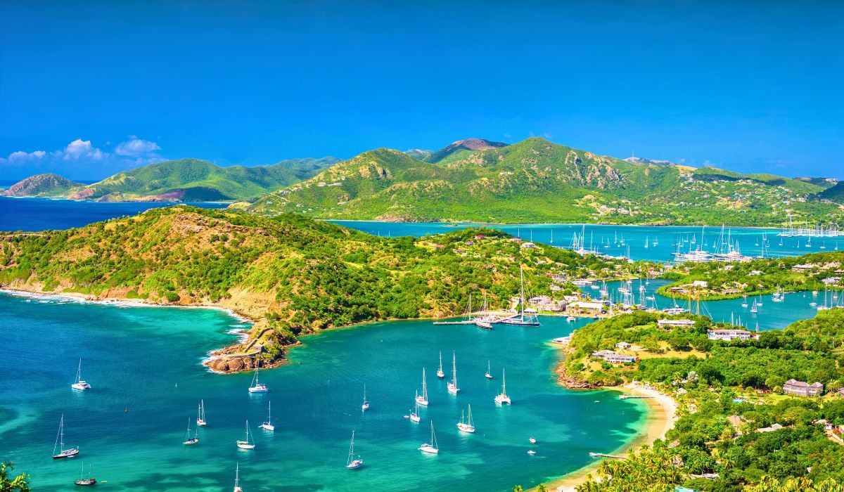 Scenic coastline of Antigua with lush green hills, vibrant blue waters, and numerous anchored sailboats.