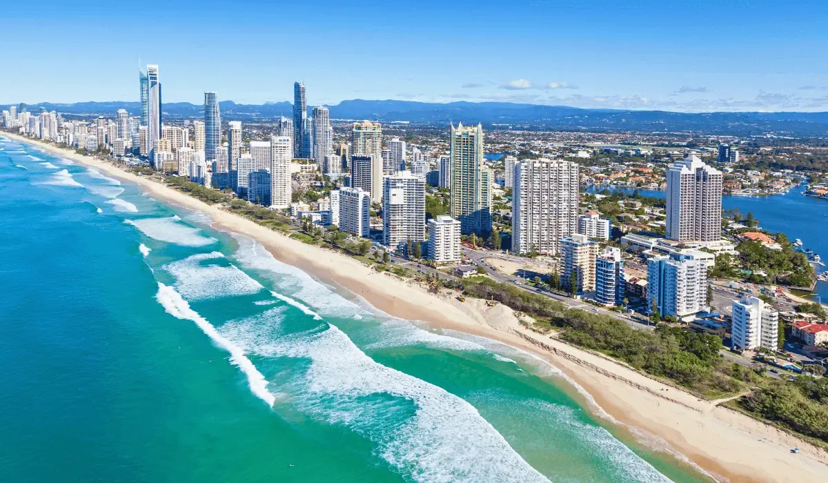Aerial view of a modern Australian coastal city with high-rise buildings and a long sandy beach, representing international property investment or lifestyle transfers in Australia