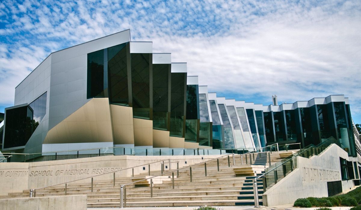 Contemporary glass and metal design of the John Curtin School of Medical Research at Australian National University under a partly cloudy sky.