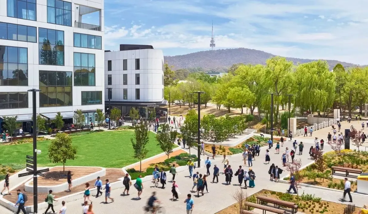 An aerial shot of the Australian National University campus in Canberra, showcasing modern academic buildings interspersed with tree-lined pathways and open green spaces.