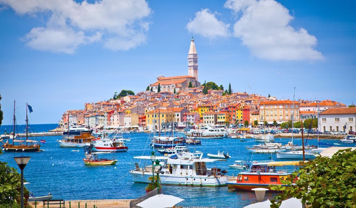 Harborfront of Rovinj, Croatia with pastel buildings and fishing boats under a clear blue sky.