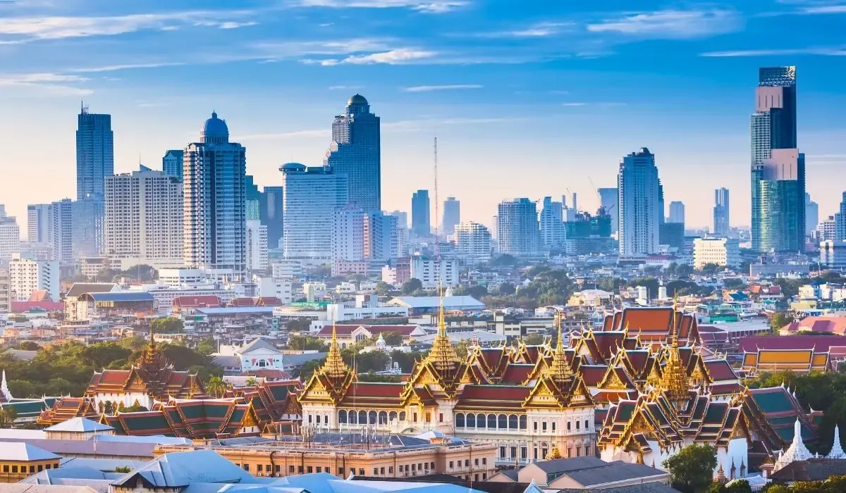 A nighttime view of Bangkok's skyline, illuminated with skyscrapers, the Chao Phraya River, and bustling city lights reflecting off the water.