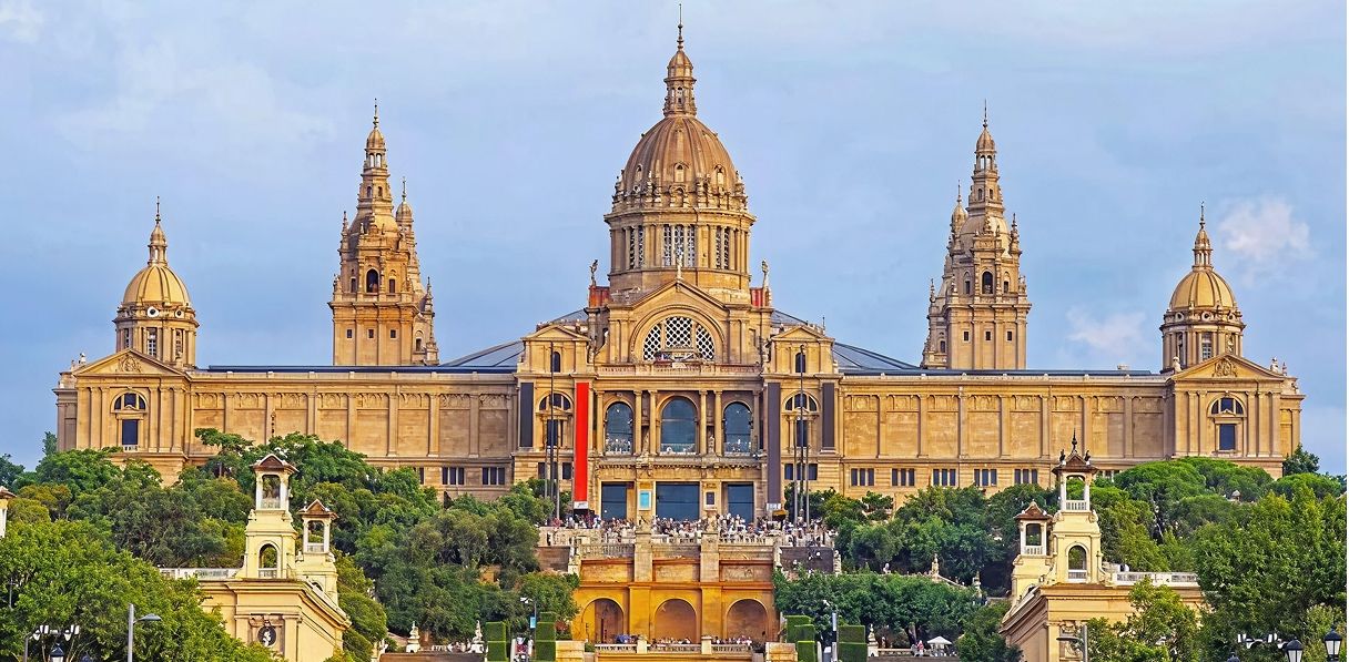 Front view of the National Art Museum of Catalonia in Barcelona, Spain, with cars parked along a wide avenue.