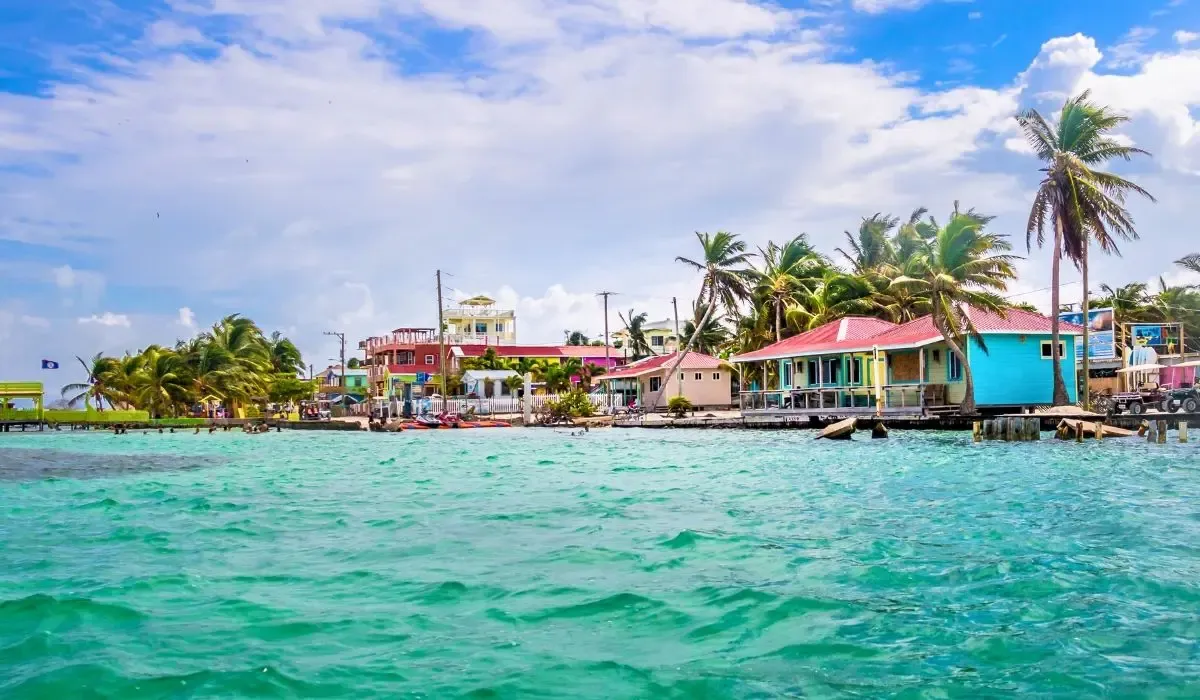 A tranquil view of Ambergris Caye in Belize, featuring overwater bungalows, calm blue waters, and a wooden pier extending into the sea.