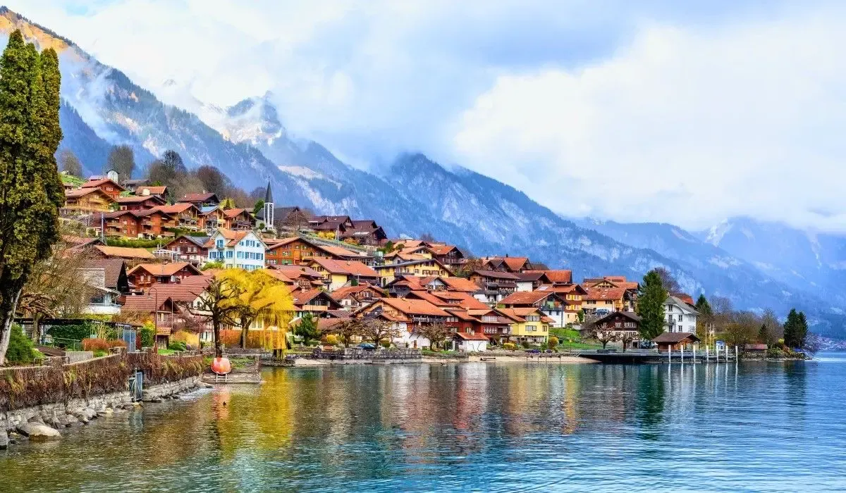 Quaint lakeside village in the Bernese Oberland, Switzerland with traditional alpine homes and dramatic snow-capped mountains in the background. Canadians purchasing property in Switzerland can leverage favorable CAD to CHF exchange rates and low transfer costs with MTFX.