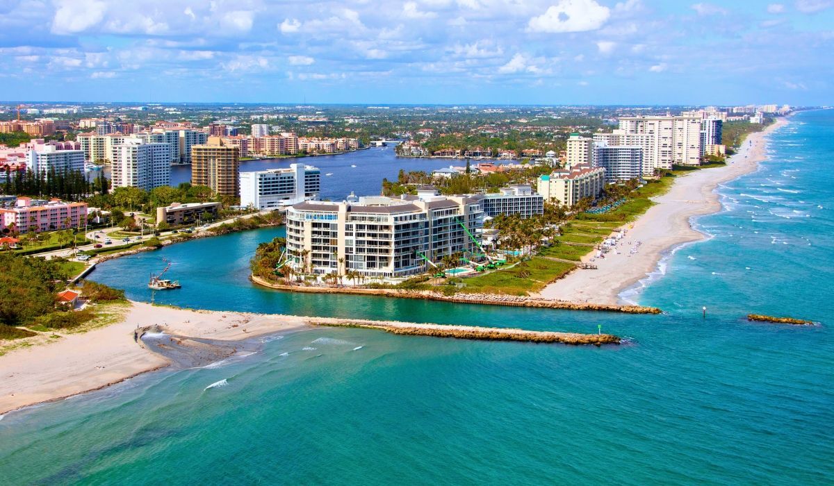A scenic coastal view of Boca Raton, Florida, showcasing sandy beaches, turquoise waters, and palm trees lining the shore under a sunny sky.