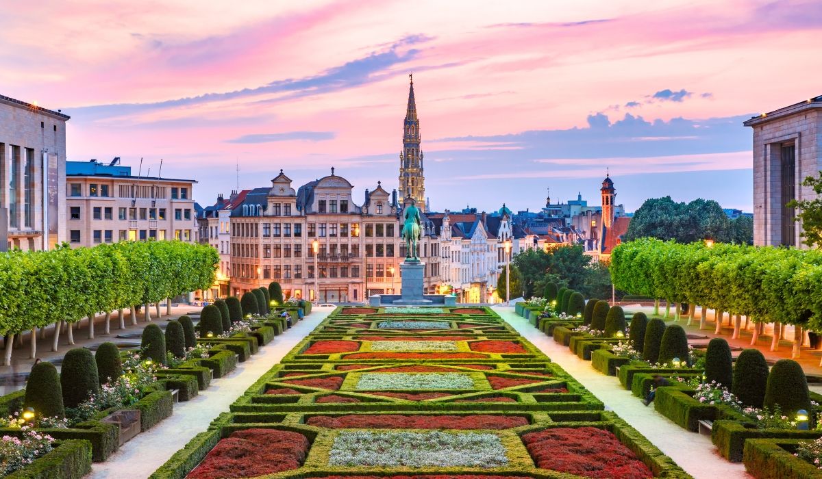 Sunset view of Brussels’ Mont des Arts garden with manicured flowerbeds, statues, and historic buildings in the background.