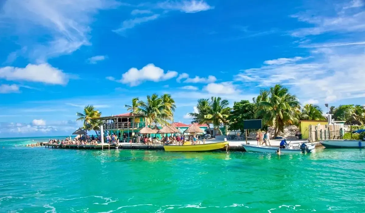 A picturesque view of Caye Caulker, Belize with colorful boats, palm trees, and people relaxing near the water.