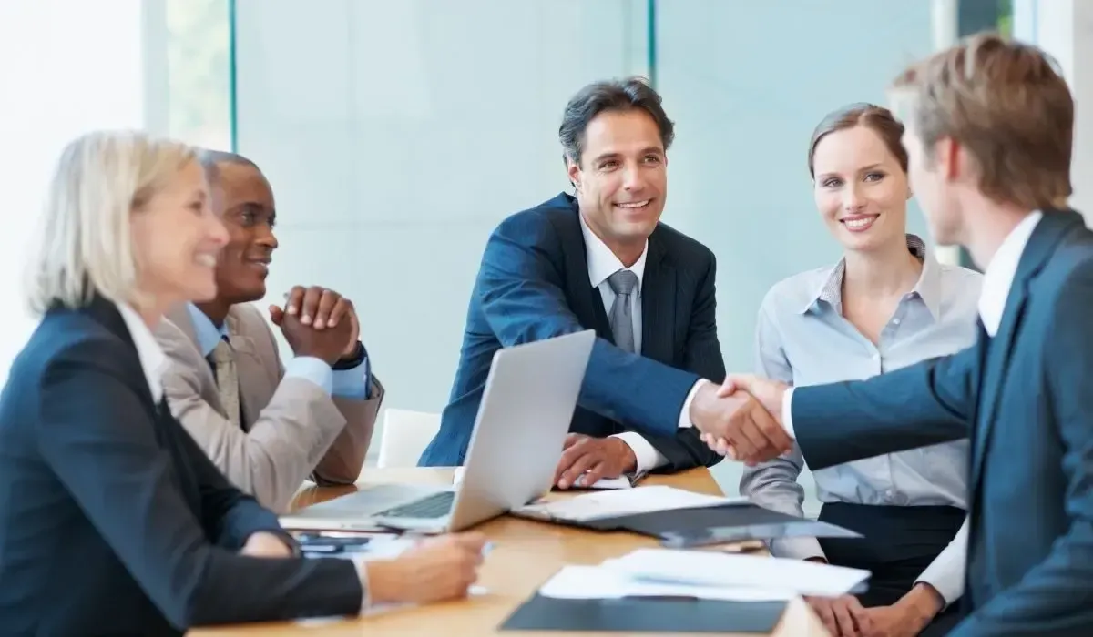 Business people shaking hands in a conference room with smiles on their faces.