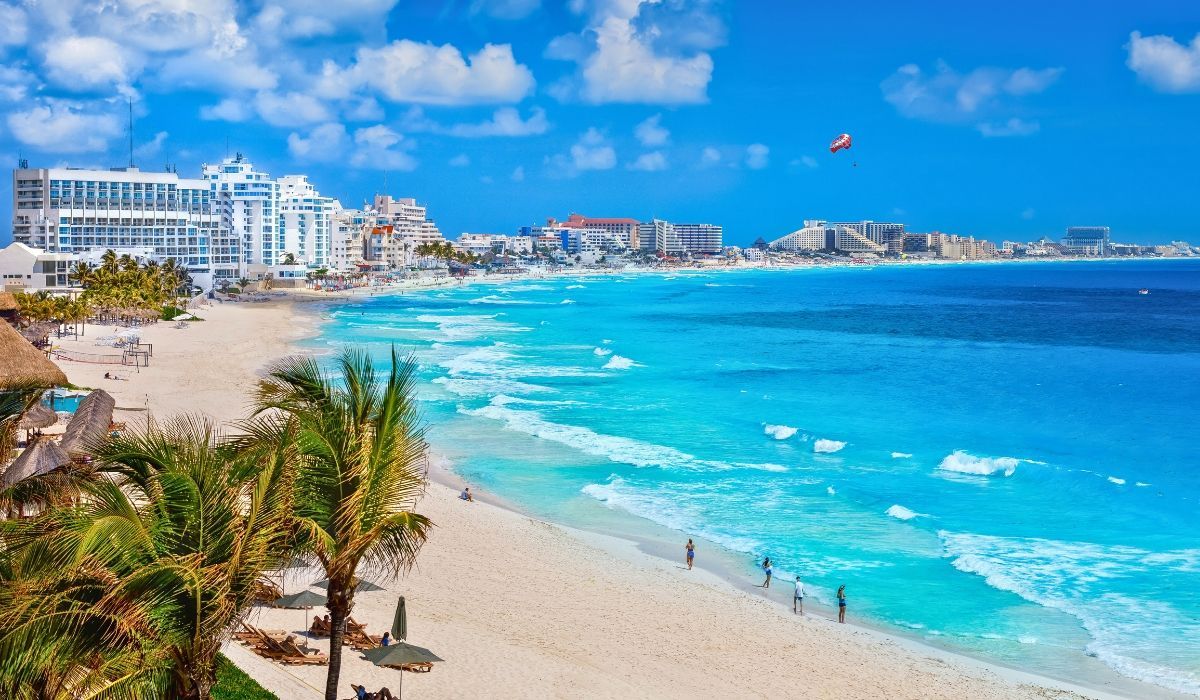 A panoramic view of Cancun's coastline, featuring white sandy beaches, turquoise waters, and high-rise resorts under a clear blue sky.